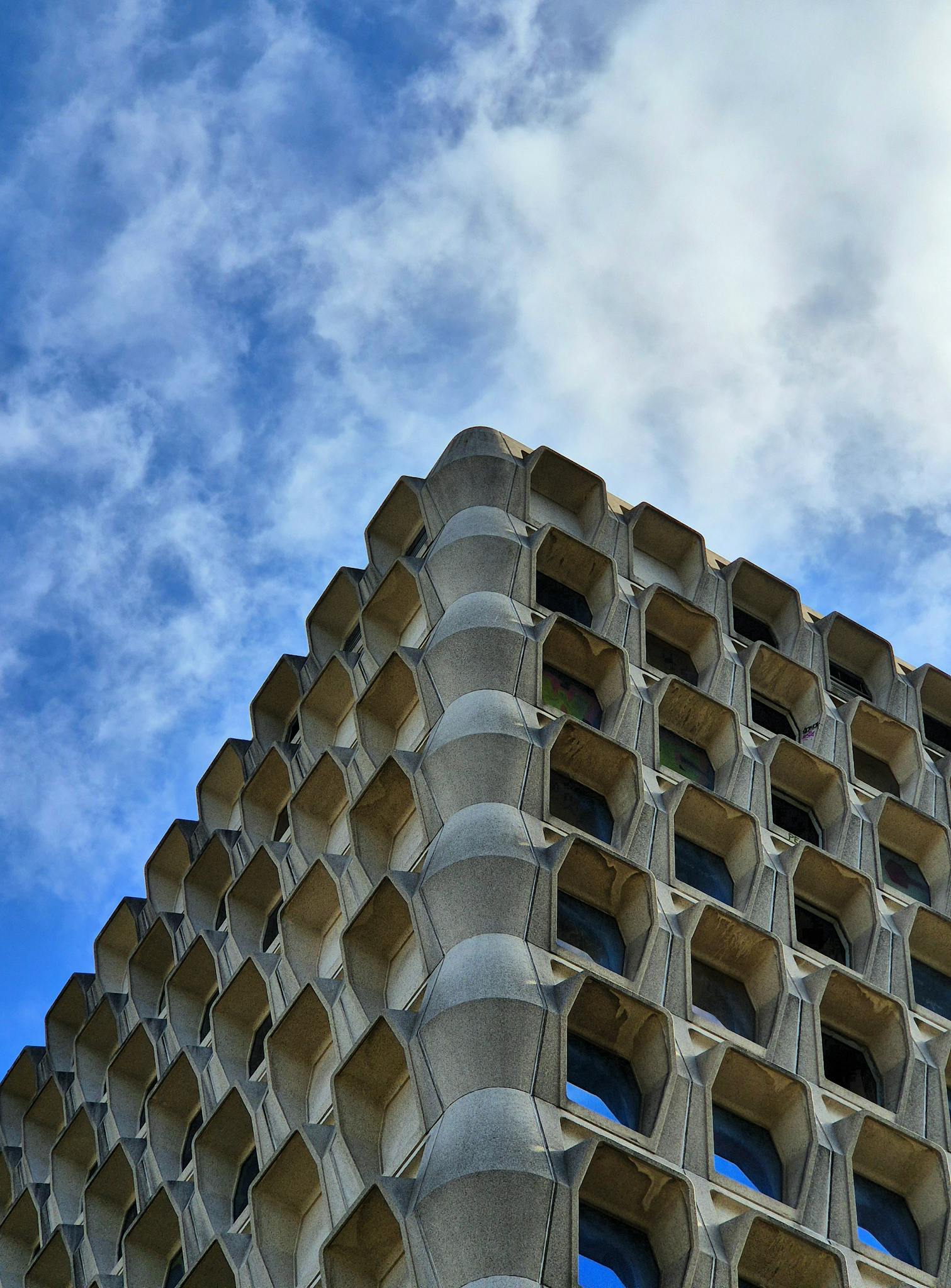 Modern building with geometric design against a vibrant blue sky and clouds.